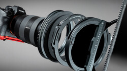 Sony mirrorless camera with multiple lens filters and adapters arranged in front of it against a gray background.