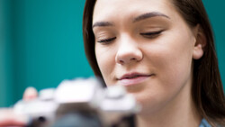 Woman with eyes closed against turquoise background, with blurred camera equipment visible behind her.