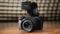 Canon EOS R5 mirrorless camera with external recorder mounted on top, positioned on wooden surface.
