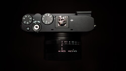 Top-down view of a rangefinder camera with dark gray body, showing dials, shutter button, and attached black lens.