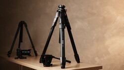 Professional tripod with ball head and video camera on wooden surface against warm backdrop.