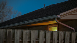 Wooden fence with illuminated house structure at dusk under deep blue twilight sky.