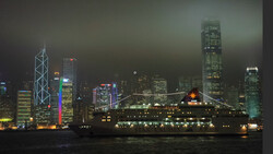 Night cityscape with illuminated skyscrapers reflected in dark water below.