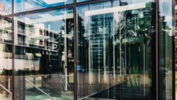 Modern glass storefront with reflections of surrounding buildings and trees on transparent panels.