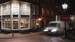 Historic European street at night with illuminated storefront and moving vehicle with motion blur.