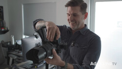Photographer holding a professional cinema camera with a large lens attachment in a bright studio setting.