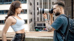 Photographer with telephoto lens photographing a woman in athletic wear on an urban rooftop.