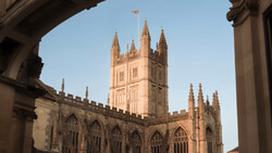 Gothic cathedral tower framed by classical stone archway, photographed during golden hour.