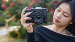 Young woman holding a mirrorless camera with a telephoto lens, looking down at the viewfinder.