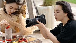 Food photographer captures a styled arrangement of fresh produce and strawberries using a professional DSLR camera.