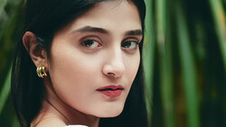 Portrait of a young woman with dark hair and gold ear cuffs against a blurred green background.
