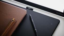 Brown leather notebook with stylus pen and digital tablet on white desk surface.