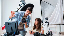 Two photographers in a studio setting with professional lighting equipment and cameras on a desk.