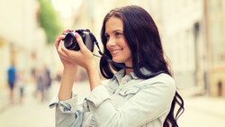 Woman holding binoculars up to her eyes while smiling at the camera on an urban street.