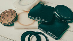 Collection of dark teal and rose gold photography equipment and accessories arranged on a white wooden surface.