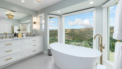 Modern bathroom with freestanding white oval tub positioned in front of large windows overlooking green hillside landscape.