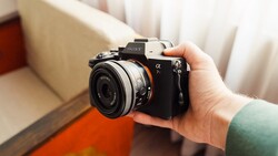 Hand holding a Sony Alpha mirrorless camera with a compact prime lens attached, indoors.