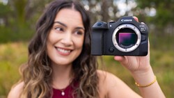 Woman holding Canon EOS R5 mirrorless camera body with sensor visible in outdoor setting.