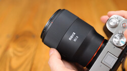 Metus 85mm lens mounted on a mirrorless camera, held in someone's hand against a warm, blurred background.
