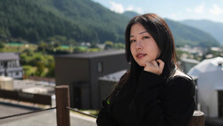 Woman in black clothing posed on a rooftop overlooking a forested valley and distant mountains.