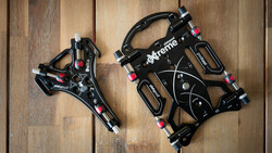 Two black mechanical disc brakes displayed on a wooden surface, showing different sizes and components.