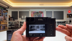 Hands holding a Leica Q camera displaying its rear LCD screen in a photography studio setting.
