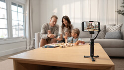 Smartphone mounted on tripod recording family playing board game at wooden table.