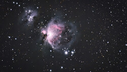The Orion Nebula glowing pink and white against a starfield, with dark dust lanes and bright central stars.