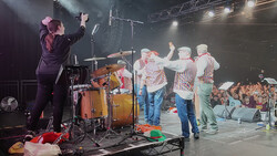 Live concert performance with band members on stage under professional lighting and rigging.