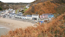 Coastal village nestled against a steep cliff with colorful beach huts and stone buildings along the shoreline.