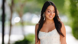 Woman in white sleeveless top looking downward with soft natural lighting in outdoor setting.