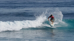 Surfer riding a turquoise wave in a red board shorts, angled into the curl of white foam.