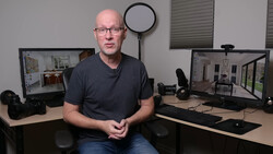 Man sitting at desk with dual monitors displaying 3D architectural renderings and professional lighting setup.