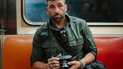 Man holding a vintage camera on public transit, wearing a green utility shirt.