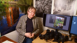 Photographer reviewing images on a monitor surrounded by camera equipment and lenses.