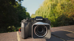 Fujifilm X-T5 camera body positioned next to a compact film camera on a road with tree-lined edges.