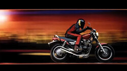 Motorcyclist in red and black leather riding a vintage cruiser motorcycle against a warm sunset gradient background.