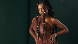 Portrait of a woman in a rust-colored draped garment against a deep green background.