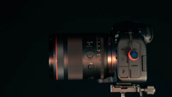 Cinema camera with interchangeable lens mounted on tripod plate, shot from above against dark background.