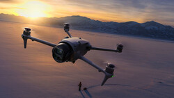 Quadcopter drone hovering above a beach at sunset with mountains in the distance.