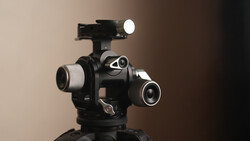 Professional cinema camera head with multiple lens ports and mounted LED light on tripod.