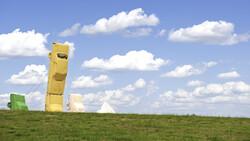 Colorful inflatable structures arranged in a grassy field under a partly cloudy blue sky.