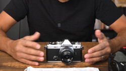 Hands presenting a vintage rangefinder camera on a wooden surface.
