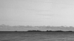 Minimalist black and white seascape with dark landmasses silhouetted against an overcast sky.