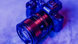 Nikon mirrorless camera with red and black lens on purple-blue gradient background.