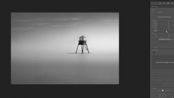 Minimalist photograph of a tall wooden structure with four spindly legs centered in an expansive, featureless gray landscape.