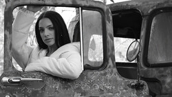Woman in white jacket leaning out of vintage truck window in black and white portrait.