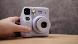 Lavender Instax Mini SE instant camera held in hand against neutral background.