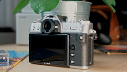 Rangefinder camera with articulating rear screen displayed on wooden desk with potted plant in background.