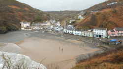 Coastal village nestled in a valley with sandy beach at low tide and residential buildings along the shoreline.